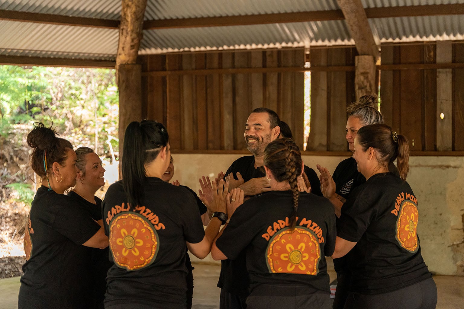 Group of male and female particiants in a small circle while a male participant stands in the middle smiling