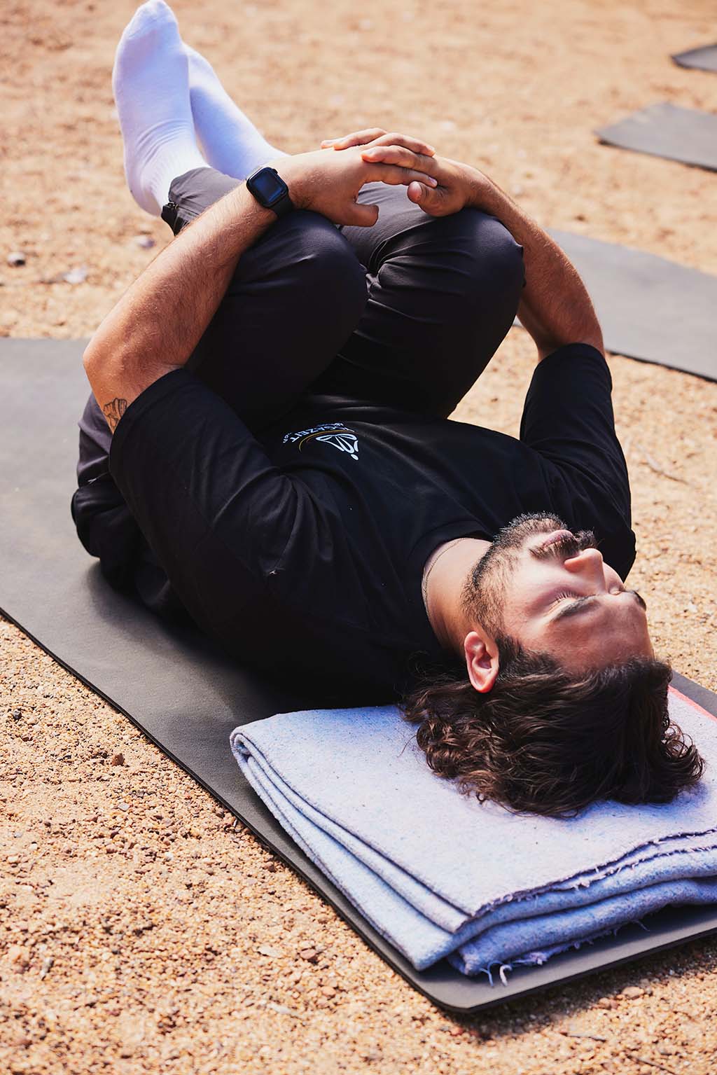 Male participant laying on yoga mat and hugging knees to their chest with their eyes closed